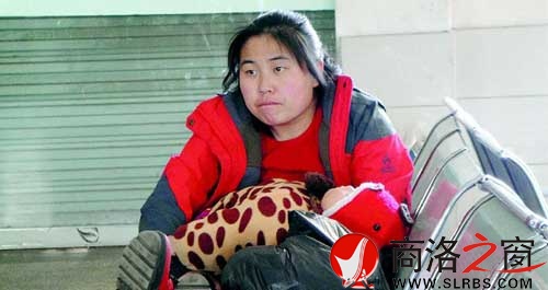 候車廳里，一位母親抱著睡著的孩子發(fā)呆
